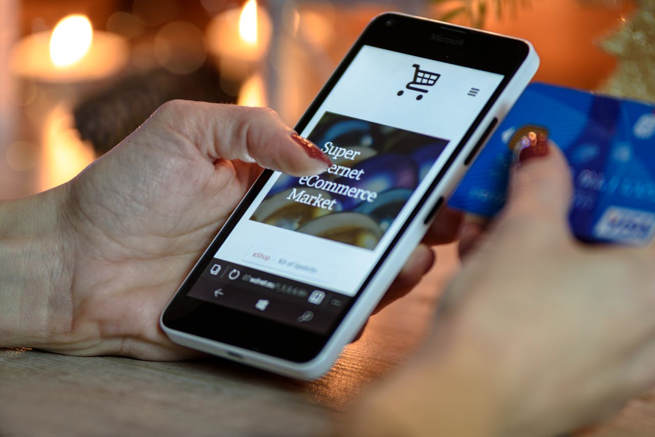 social-feed-img-02 Woman using smartphone for online shopping with credit card in hand, festive background lighting.